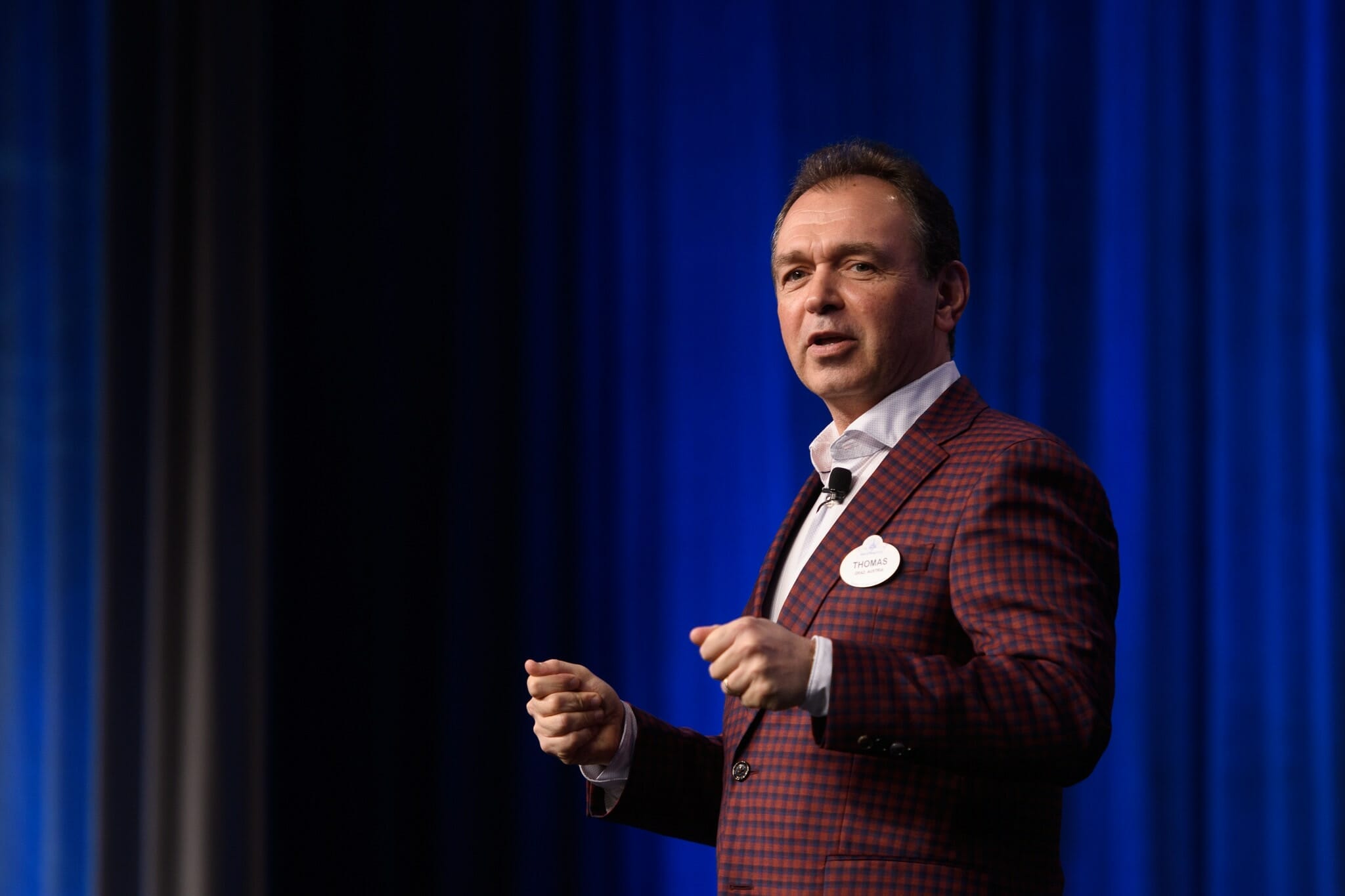 Foto de Thomas Mazloum Foto de Thomas Mazloum, representante da Disney no comitê do Orange County. Ele está em um palco falando e gesticulando.