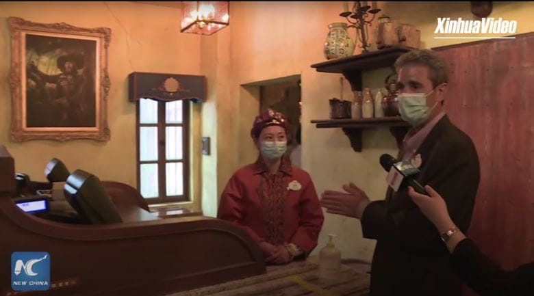 Foto de um repórter entrevistando uma atendente de caixa na Disney de Shanghai, ambos de máscara, em uma reportagem sobre a reabertura do parque 